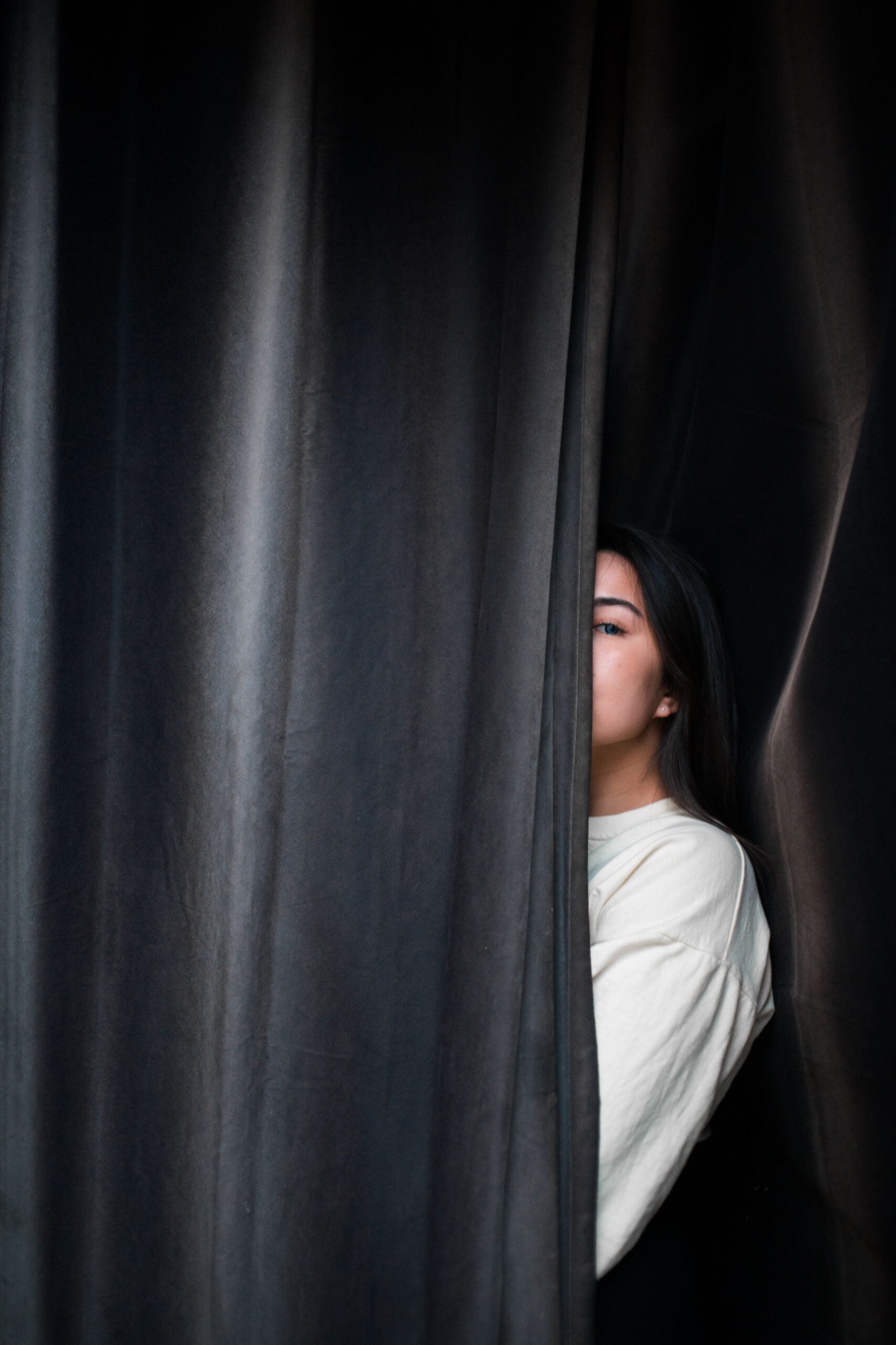 person peeking out from behind black stage curtains but not fully visible
