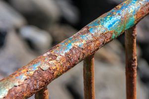 close-up of rusty fence or guard rail with flaking off layers of blue, green, and yellow paint
