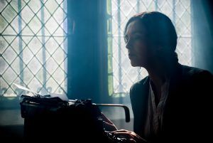 woman sitting at a typewriter in front of leaded glass windows