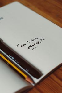 journal with pencil and pen and writing "Am I good enough?"